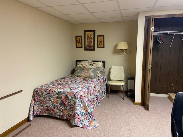 carpeted bedroom with a paneled ceiling, baseboards, and a closet