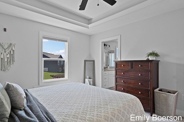 bedroom with a tray ceiling, ensuite bathroom, and a ceiling fan