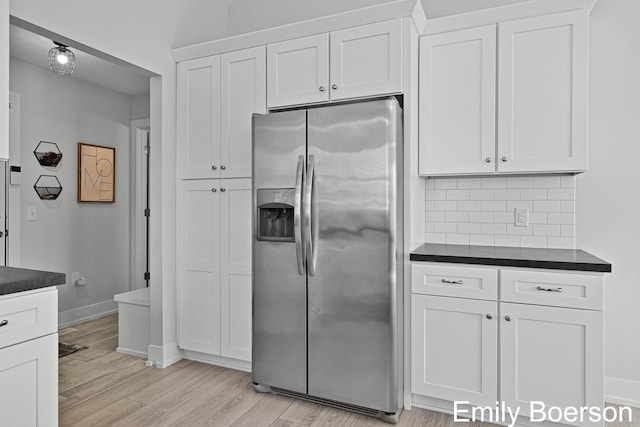 kitchen featuring light wood-style flooring, baseboards, stainless steel refrigerator with ice dispenser, backsplash, and dark countertops