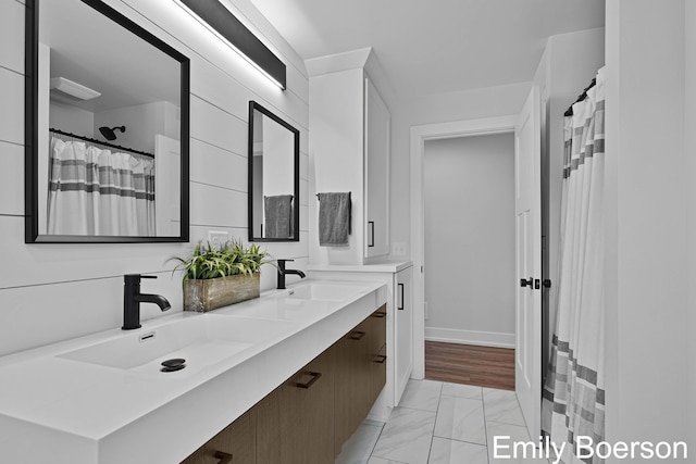 bathroom featuring baseboards, marble finish floor, double vanity, and a sink