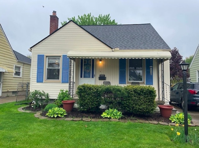 bungalow with a porch, roof with shingles, a front lawn, and a chimney