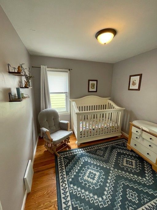bedroom with a crib, visible vents, wood finished floors, and baseboards