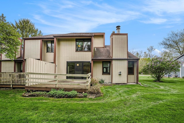 back of house with roof with shingles, a wooden deck, and a lawn