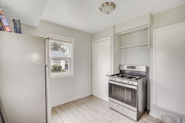 kitchen featuring stainless steel gas range, freestanding refrigerator, light wood-style flooring, baseboards, and open shelves