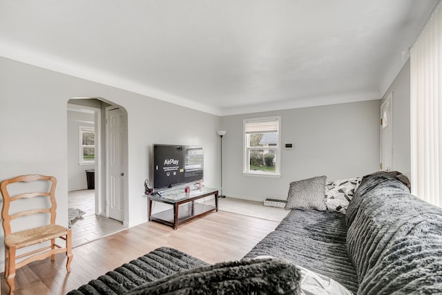 living area with arched walkways, light wood-style flooring, and baseboards
