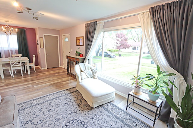 living room with rail lighting, a chandelier, baseboards, and light wood-type flooring