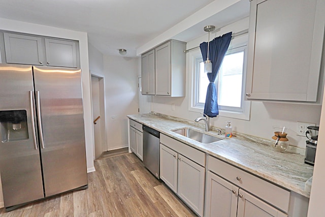 kitchen featuring appliances with stainless steel finishes, a sink, gray cabinets, light wood finished floors, and light stone countertops