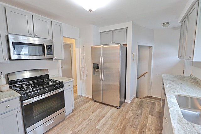 kitchen featuring appliances with stainless steel finishes, gray cabinets, light wood-style floors, a sink, and light stone countertops