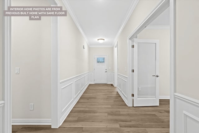 hall with crown molding, a decorative wall, a wainscoted wall, and wood finished floors
