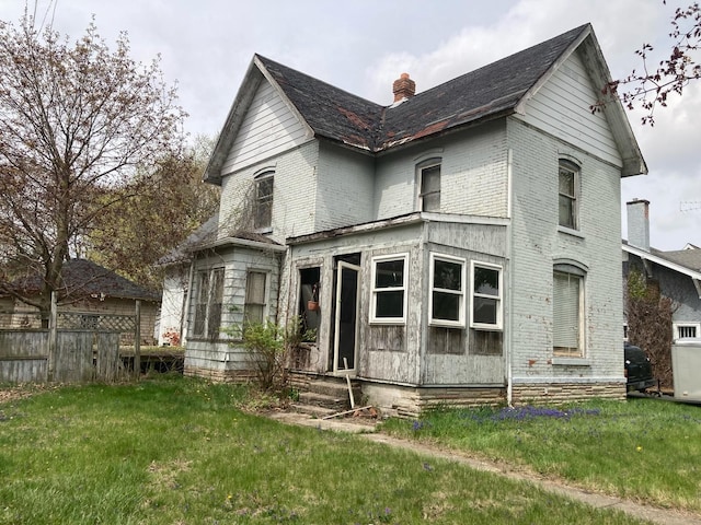 exterior space featuring a chimney, brick siding, fence, entry steps, and a front lawn