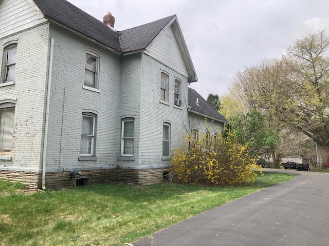 view of home's exterior featuring a chimney, brick siding, and a lawn
