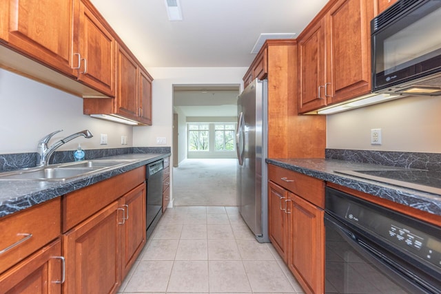kitchen with brown cabinetry, black appliances, light tile patterned floors, and a sink