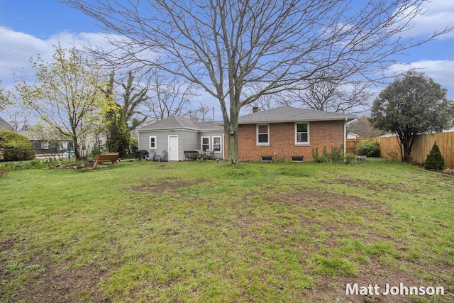 back of property with brick siding, a chimney, fence, and a lawn