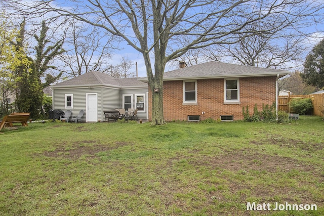 back of house with fence, a chimney, brick siding, and a lawn