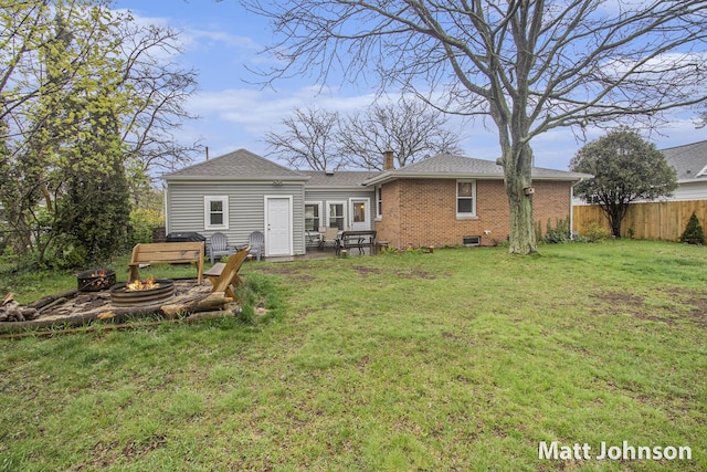 rear view of property featuring fence, a fire pit, brick siding, a yard, and a chimney