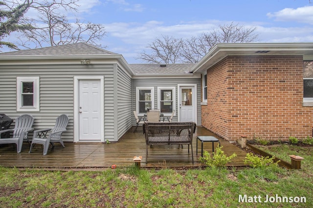 back of house featuring roof with shingles, a wooden deck, and brick siding