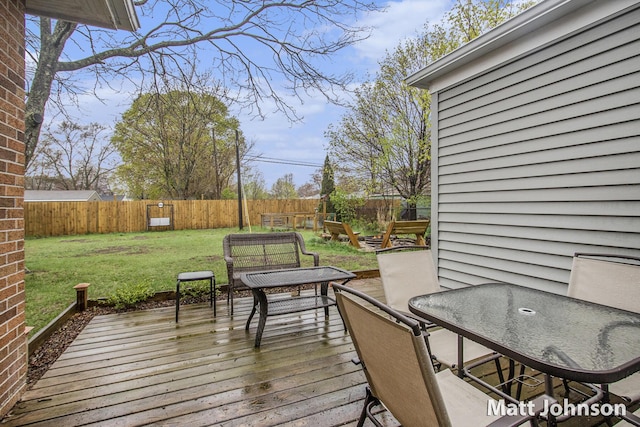 wooden terrace featuring a lawn, outdoor dining area, and a fenced backyard