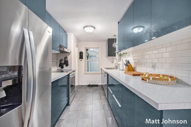kitchen featuring ventilation hood, tasteful backsplash, appliances with stainless steel finishes, and blue cabinetry