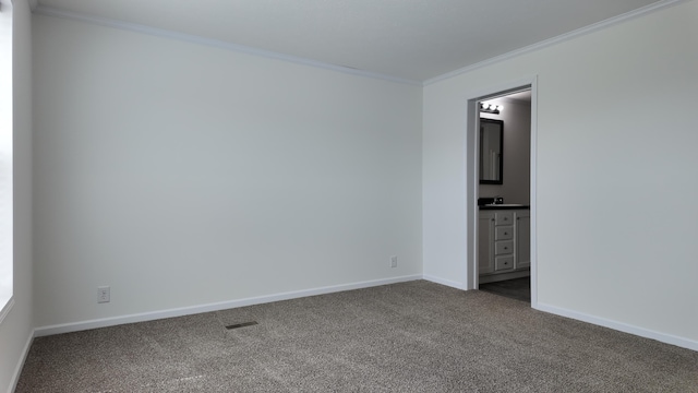 unfurnished room with a sink, visible vents, crown molding, dark colored carpet, and baseboards