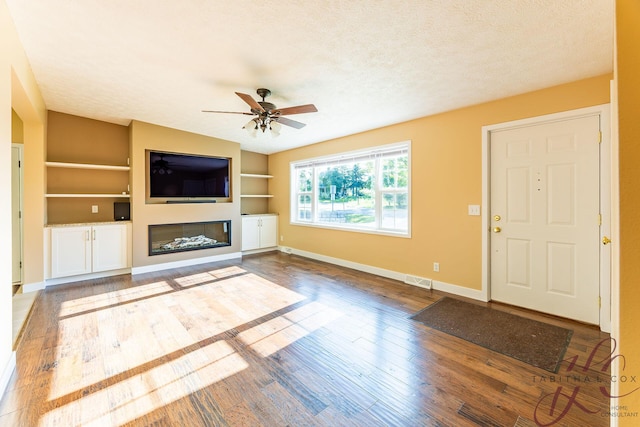 9379 Cook St, Montague, MI 49437 - unfurnished living room with built in shelves, baseboards, a ceiling fan, wood finished floors, and a glass covered fireplace