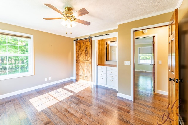 9379 Cook St, Montague, MI 49437 - unfurnished bedroom featuring a barn door, wood finished floors, ornamental molding, baseboards, and a textured ceiling