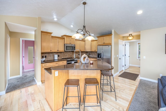 kitchen featuring a kitchen bar, light wood-style floors, a kitchen island with sink, appliances with stainless steel finishes, and tasteful backsplash