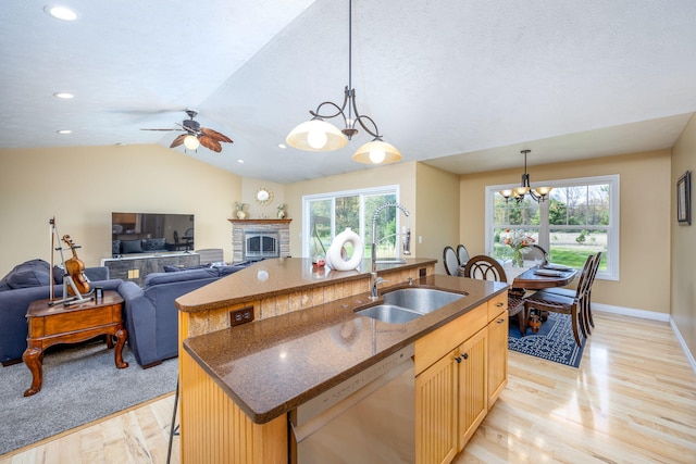 kitchen featuring stainless steel dishwasher, a sink, a kitchen island with sink, light wood-style floors, and a fireplace