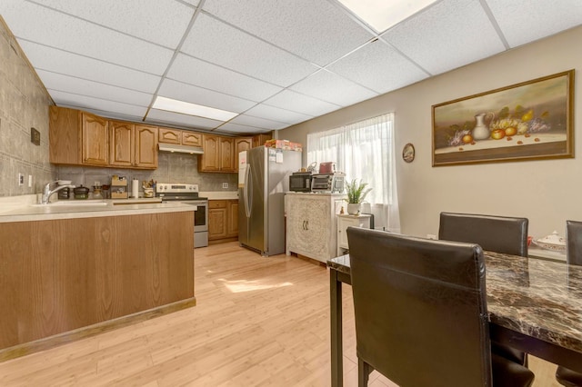 kitchen with appliances with stainless steel finishes, a sink, under cabinet range hood, light wood-style flooring, and brown cabinets