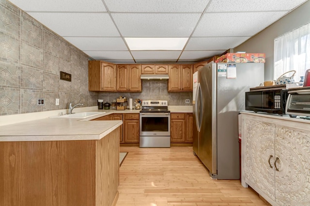 kitchen featuring appliances with stainless steel finishes, a sink, a paneled ceiling, light wood finished floors, and brown cabinetry
