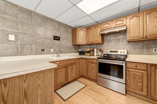 kitchen with stainless steel electric stove, under cabinet range hood, a sink, a drop ceiling, and light countertops