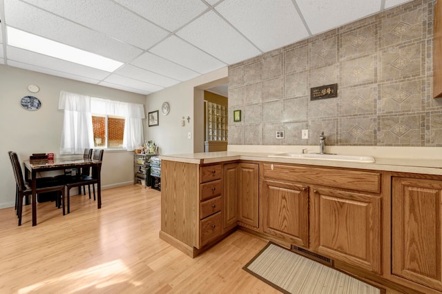kitchen featuring a sink, light wood-type flooring, light countertops, brown cabinetry, and a peninsula