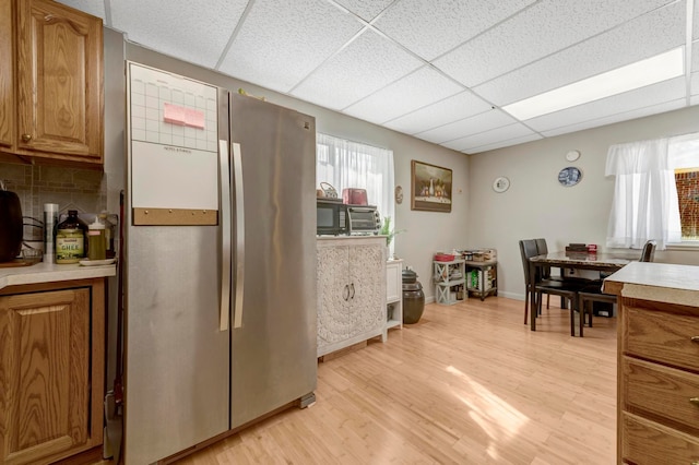 kitchen with freestanding refrigerator, a paneled ceiling, light countertops, light wood-type flooring, and brown cabinets