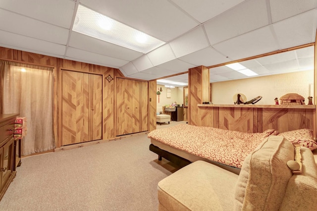 living area featuring wooden walls, a drop ceiling, and carpet flooring