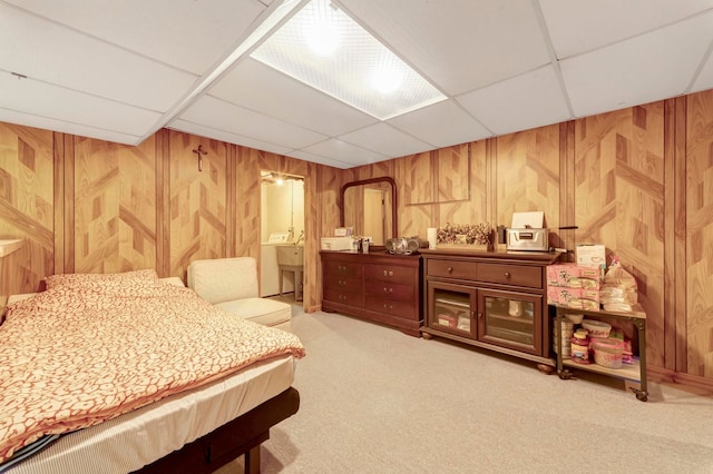bedroom with a drop ceiling, wooden walls, and light carpet