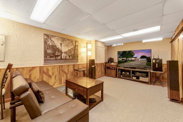 carpeted living area with a paneled ceiling, a textured wall, wooden walls, and a wainscoted wall