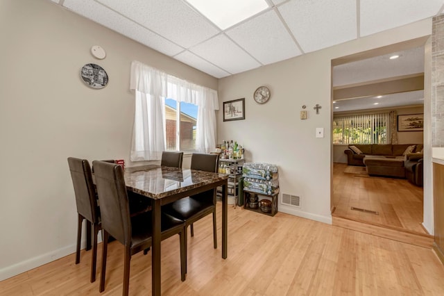 dining room featuring light wood-style flooring, a drop ceiling, and baseboards