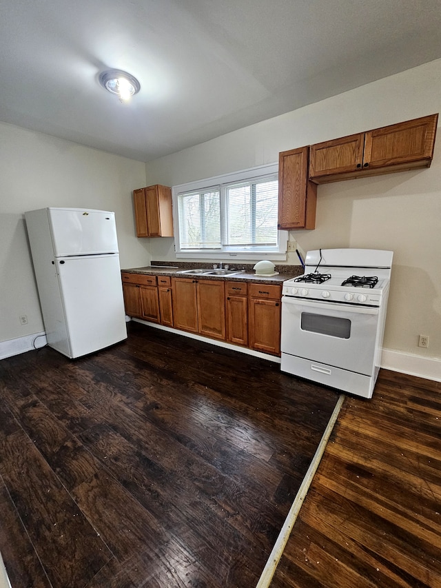 kitchen featuring brown cabinetry, white appliances, dark wood-style floors, baseboards, and dark countertops
