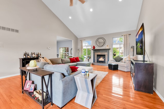 living area featuring high vaulted ceiling, ceiling fan, light wood-type flooring, a tiled fireplace, and recessed lighting