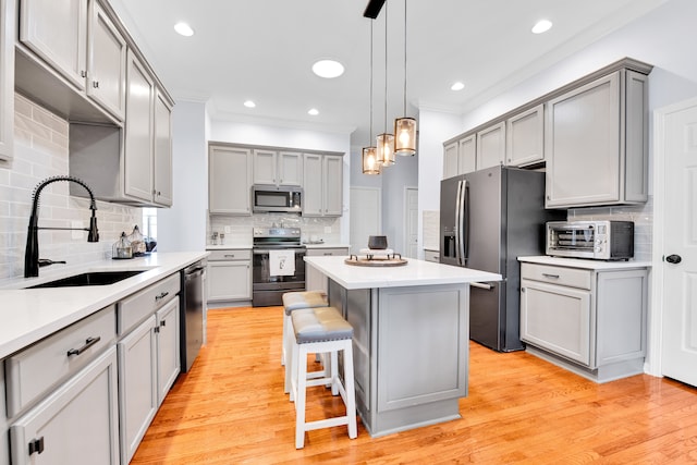 kitchen with stainless steel appliances, a sink, gray cabinets, ornamental molding, and decorative backsplash