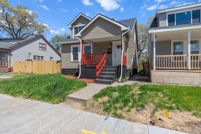 bungalow-style home with a porch, a shingled roof, and fence