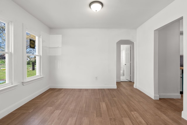 empty room featuring arched walkways, wood finished floors, and baseboards