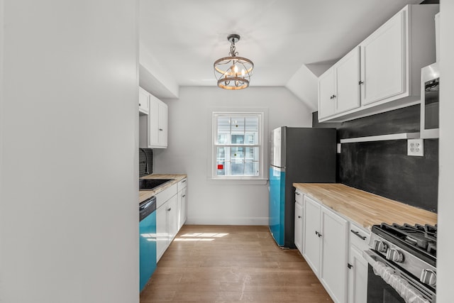 kitchen with appliances with stainless steel finishes, a chandelier, light wood-style floors, baseboards, and white cabinetry