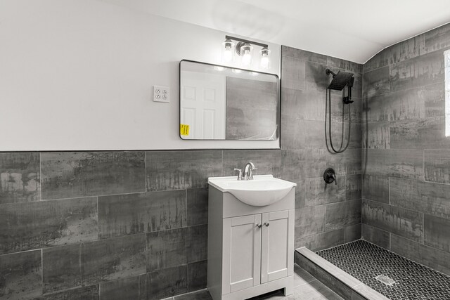 full bath with a tile shower, vanity, and tile walls