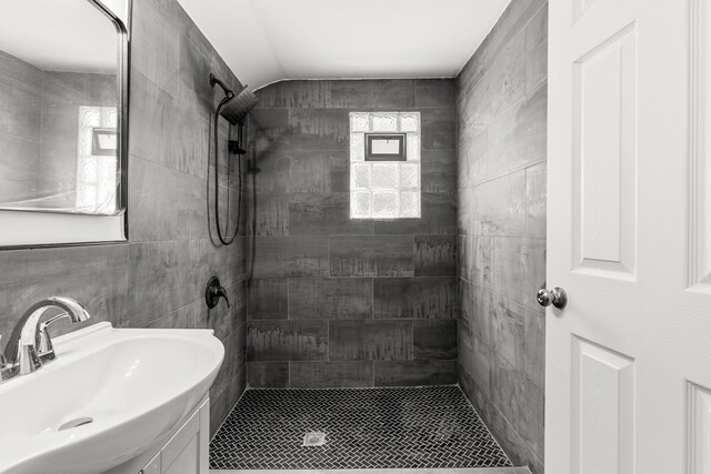 full bathroom featuring a sink, tiled shower, tile walls, and vaulted ceiling