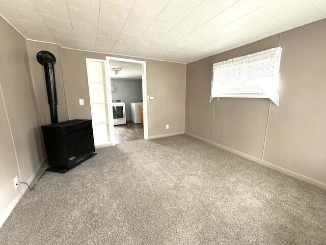 unfurnished bedroom featuring baseboards, a wood stove, independent washer and dryer, and carpet