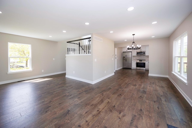 unfurnished living room featuring a wealth of natural light, a notable chandelier, dark wood finished floors, and visible vents