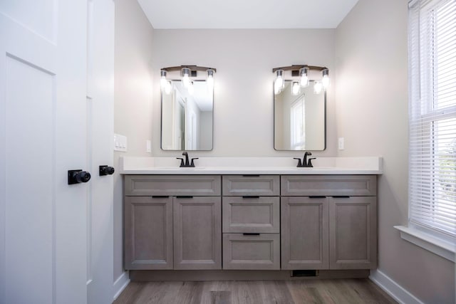 full bathroom featuring double vanity, wood finished floors, baseboards, and a sink