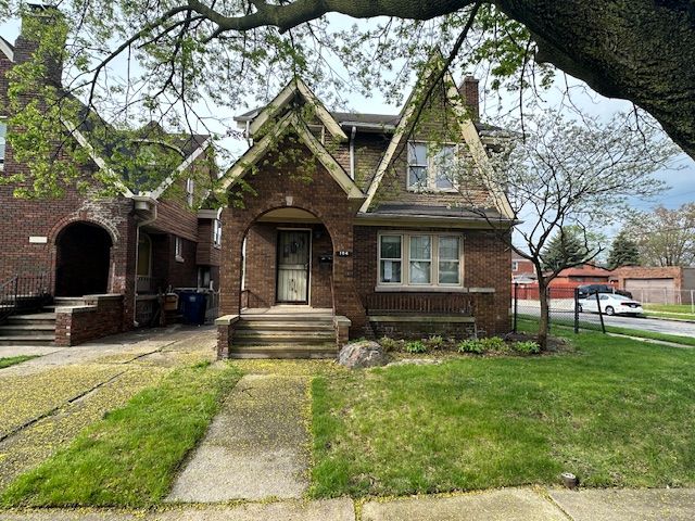 tudor home with a chimney, brick siding, and a front lawn