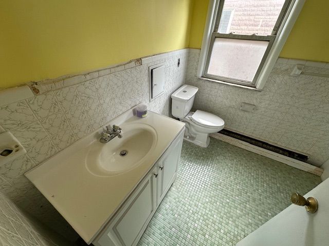 bathroom with toilet, tile patterned floors, tile walls, wainscoting, and vanity