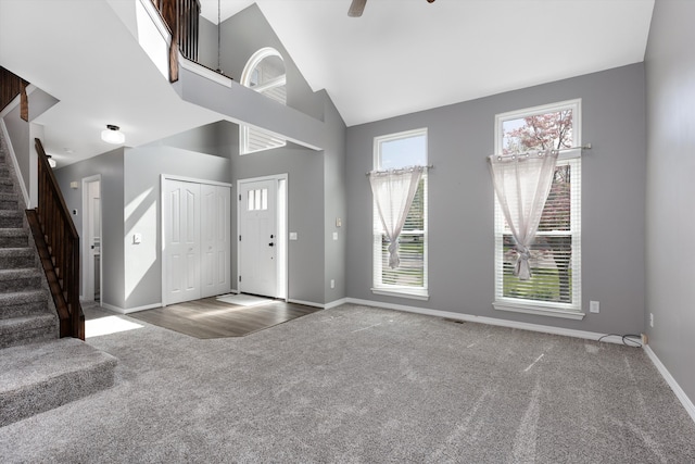 entryway with carpet floors, stairs, baseboards, high vaulted ceiling, and a ceiling fan
